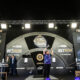 Luke Littler lifts the 2024 BetMGM Premier League Darts trophy on stage