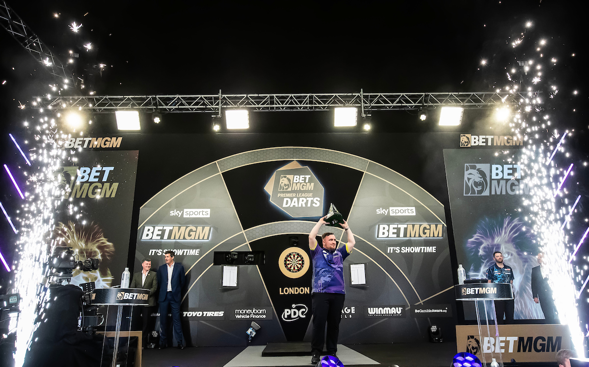 Luke Littler lifts the 2024 BetMGM Premier League Darts trophy on stage