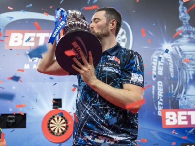 Luke Humphries holding the Phil Taylor Trophy aloft on stage at the Winter Gardens after winning the 2024 World Matchplay darts tournament. He will try and do it again at the 2026 World Matchplay
