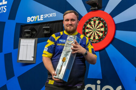 Luke Littler holding the World Grand Prix trophy on stage