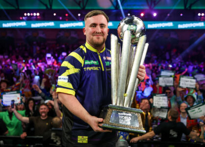 Luke Littler holding the Paddy Power World Darts Championship on stage.